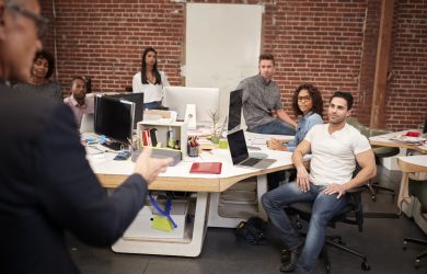 Senior Businessman Talking At Meeting Of Casually Dressed Business Team In Open Plan Office